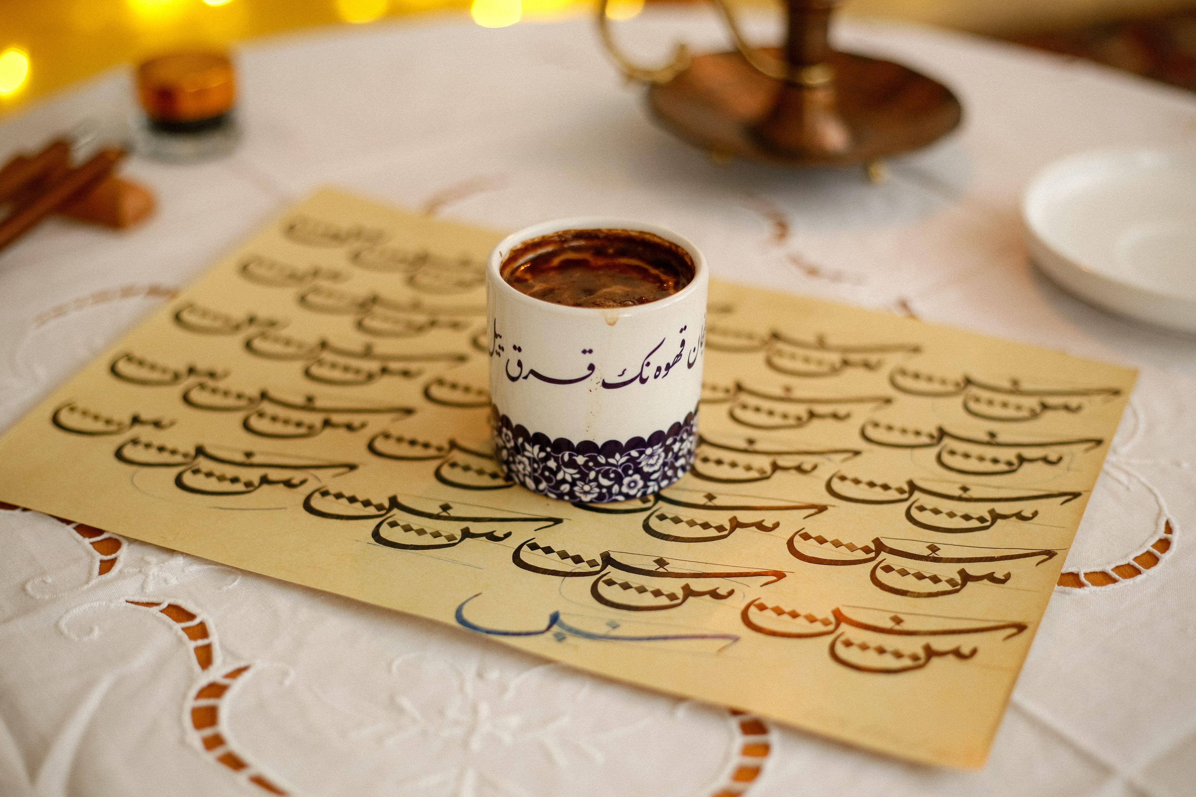 A beautifully decorated coffee cup placed on paper with elegant calligraphy, creating a warm ambiance.