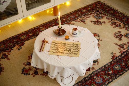Free Warm indoor scene of a table setup for calligraphy, featuring a candle, tea cup, and paper with beautiful lettering. Stock Photo