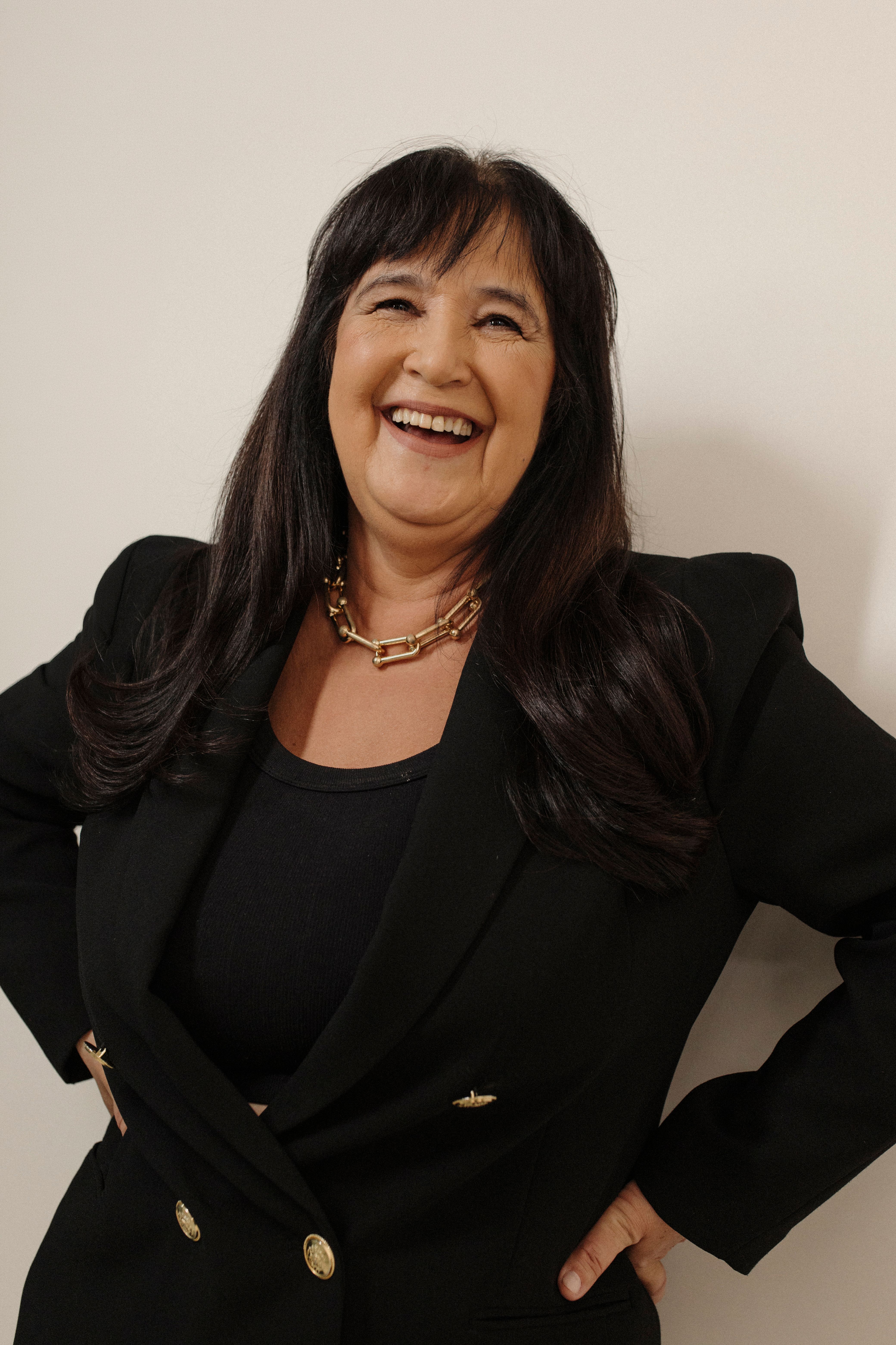 Smiling woman in a black blazer posing confidently against a neutral background.
