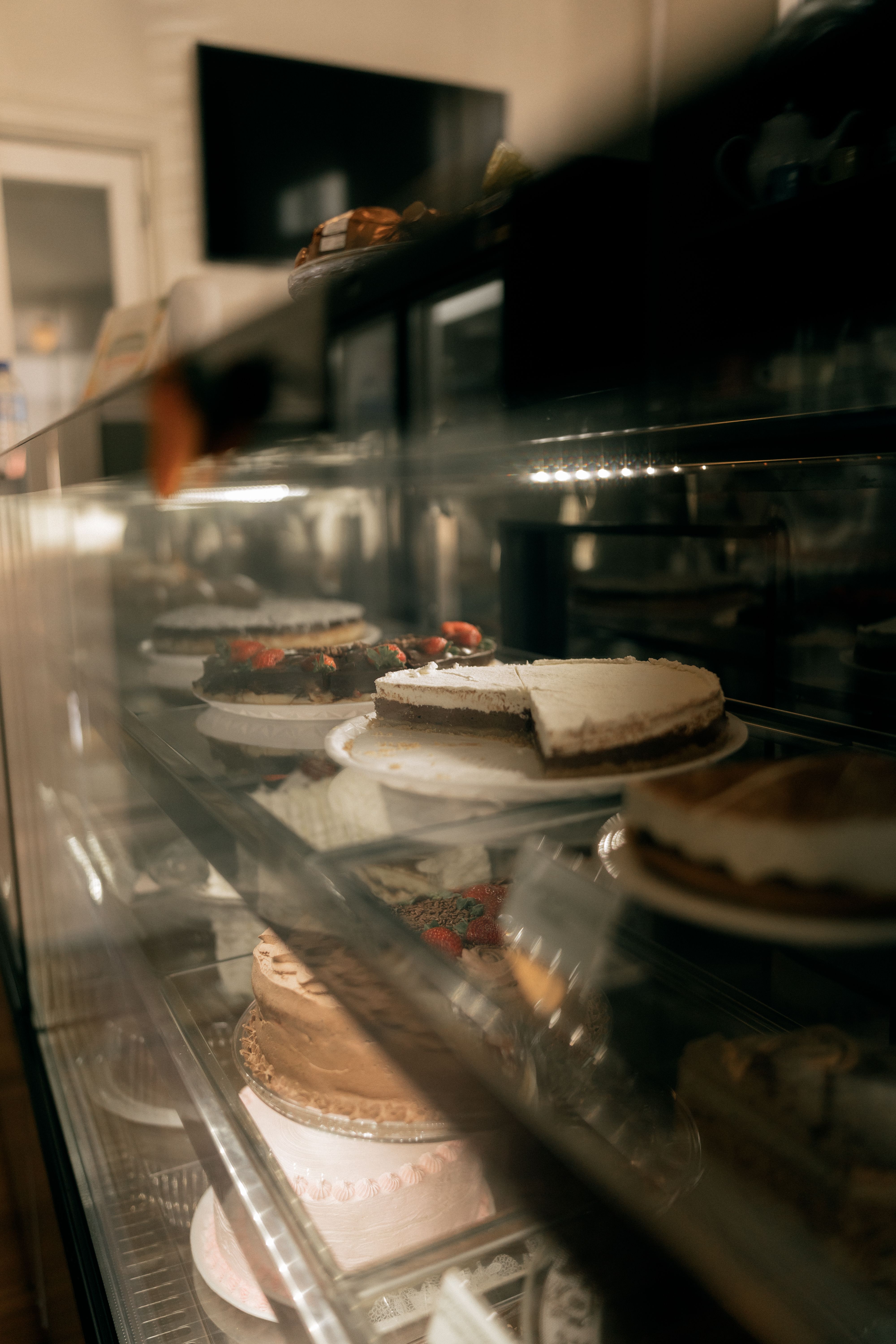 Assorted cakes in a bakery display case with soft lighting and glass reflections.