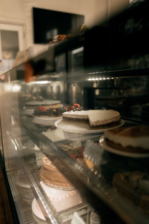 Free Assorted cakes in a bakery display case with soft lighting and glass reflections. Stock Photo