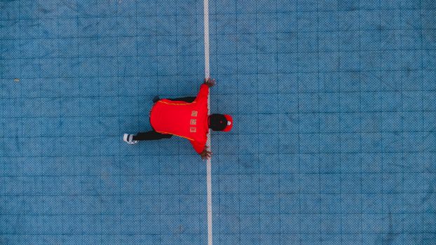 Dynamic aerial photo of a person in a red shirt on a blue outdoor court in Abuja.