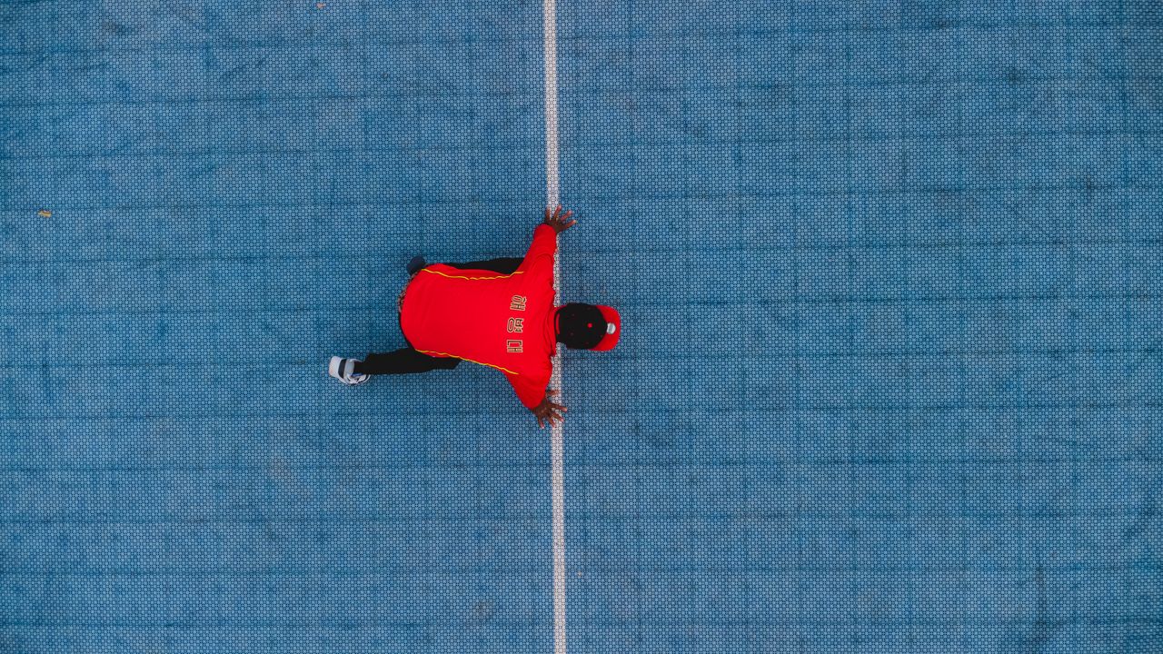 dynamic aerial photo of a person in a red shirt on a blue outdoor cour