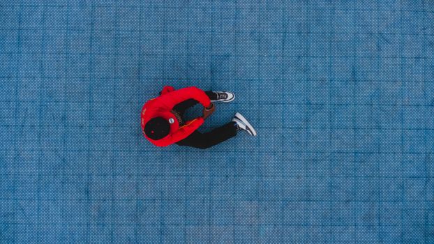 Aerial shot of a person in a red jacket sitting on a textured blue surface, creating a vivid contrast.