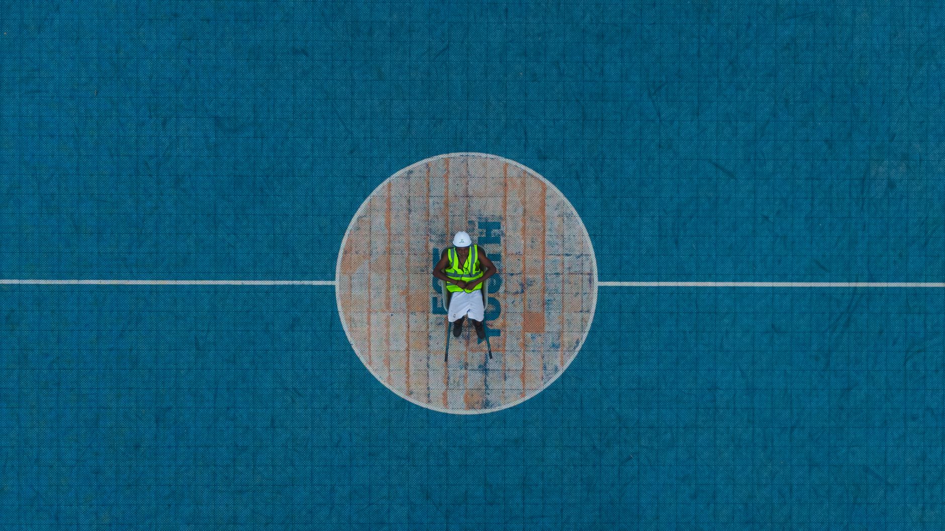 Aerial shot of a worker in safety gear standing at the center of a basketball court.