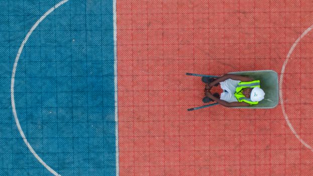 Drone shot of a worker in uniform and helmet on a colorful basketball court in Abuja, Nigeria.