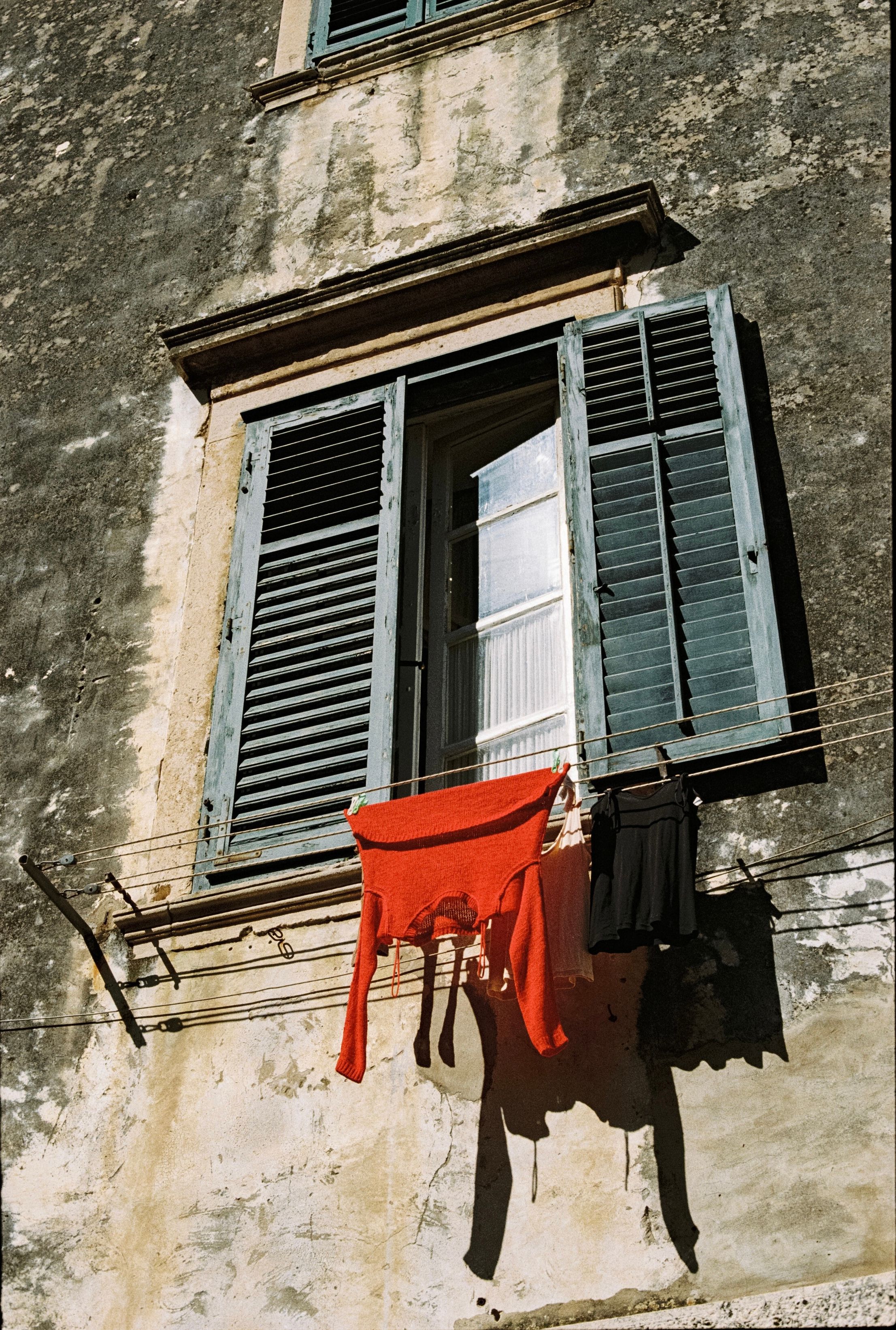 Vintage Croatian building facade with open shutters and clothes drying outside on a sunny day.