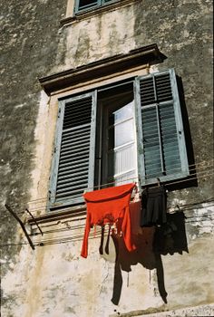 Vintage Croatian building facade with open shutters and clothes drying outside on a sunny day.
