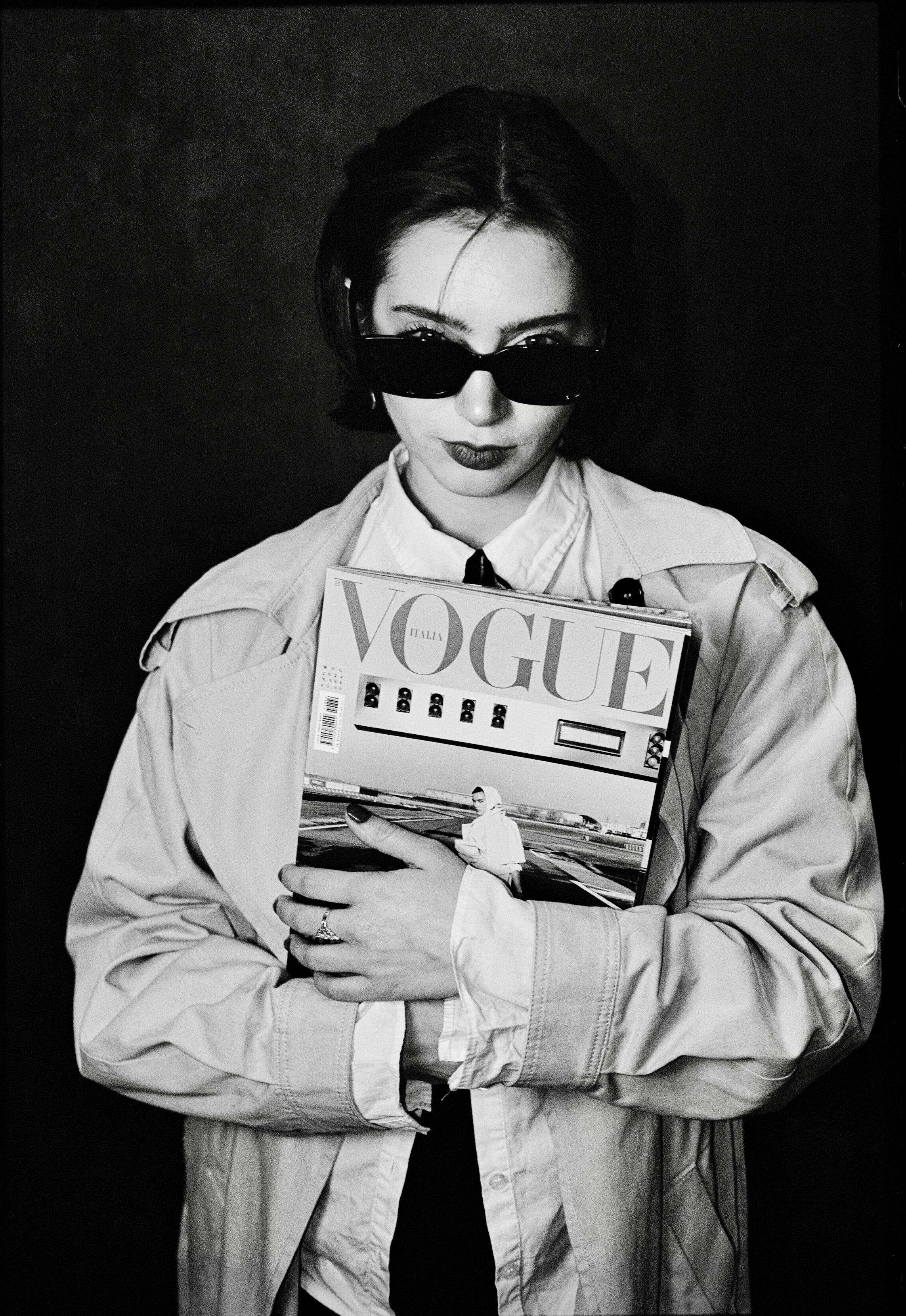 Black and white portrait of a woman in sunglasses holding a fashion magazine.