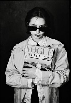 Black and white portrait of a woman in sunglasses holding a fashion magazine.