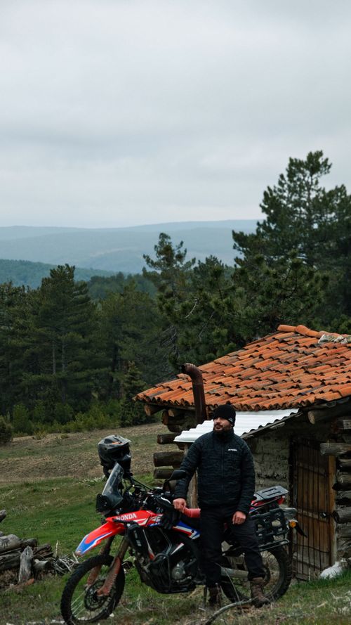 Free Man with motorcycle beside a wooden hut in a mountainous forest area. Stock Photo