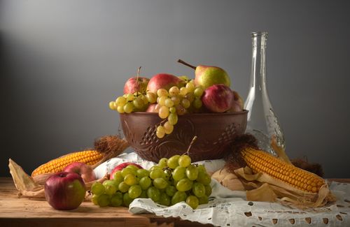 Free A classic still life featuring grapes, apples, pears, and corn in warm lighting. Stock Photo