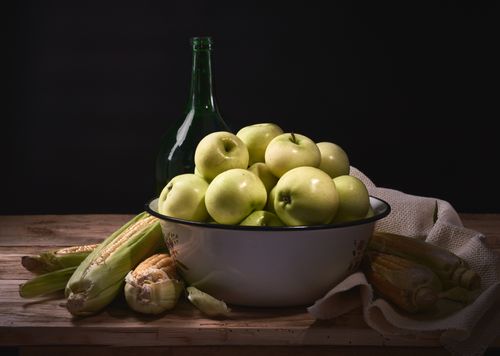 Free A rustic still life featuring a bowl of green apples and corn on a wooden table. Stock Photo