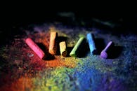 深色背景上散落着色彩缤纷的彩虹粉笔片，还带有粉笔粉