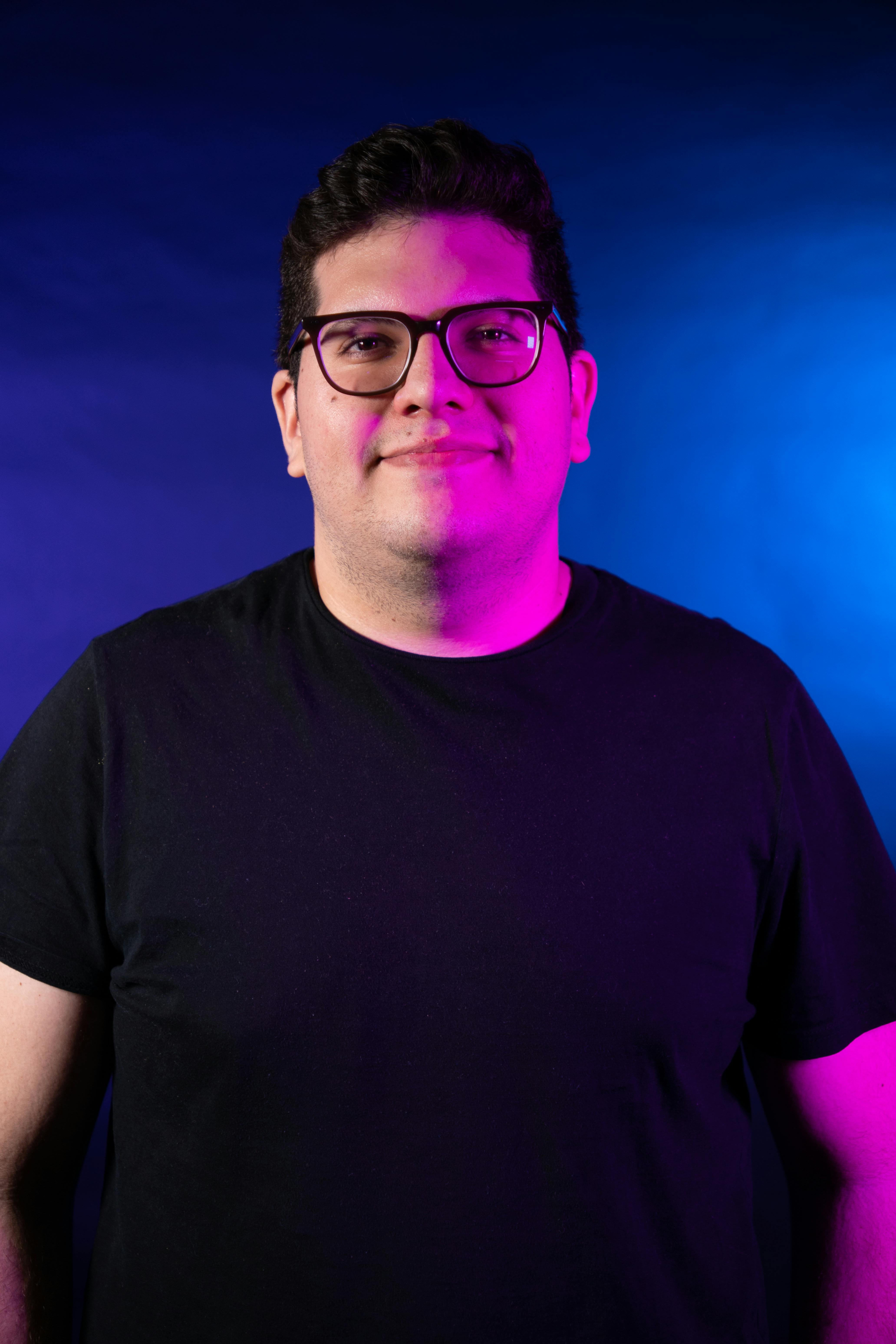 A vibrant portrait of a man smiling with dynamic purple and blue lighting.
