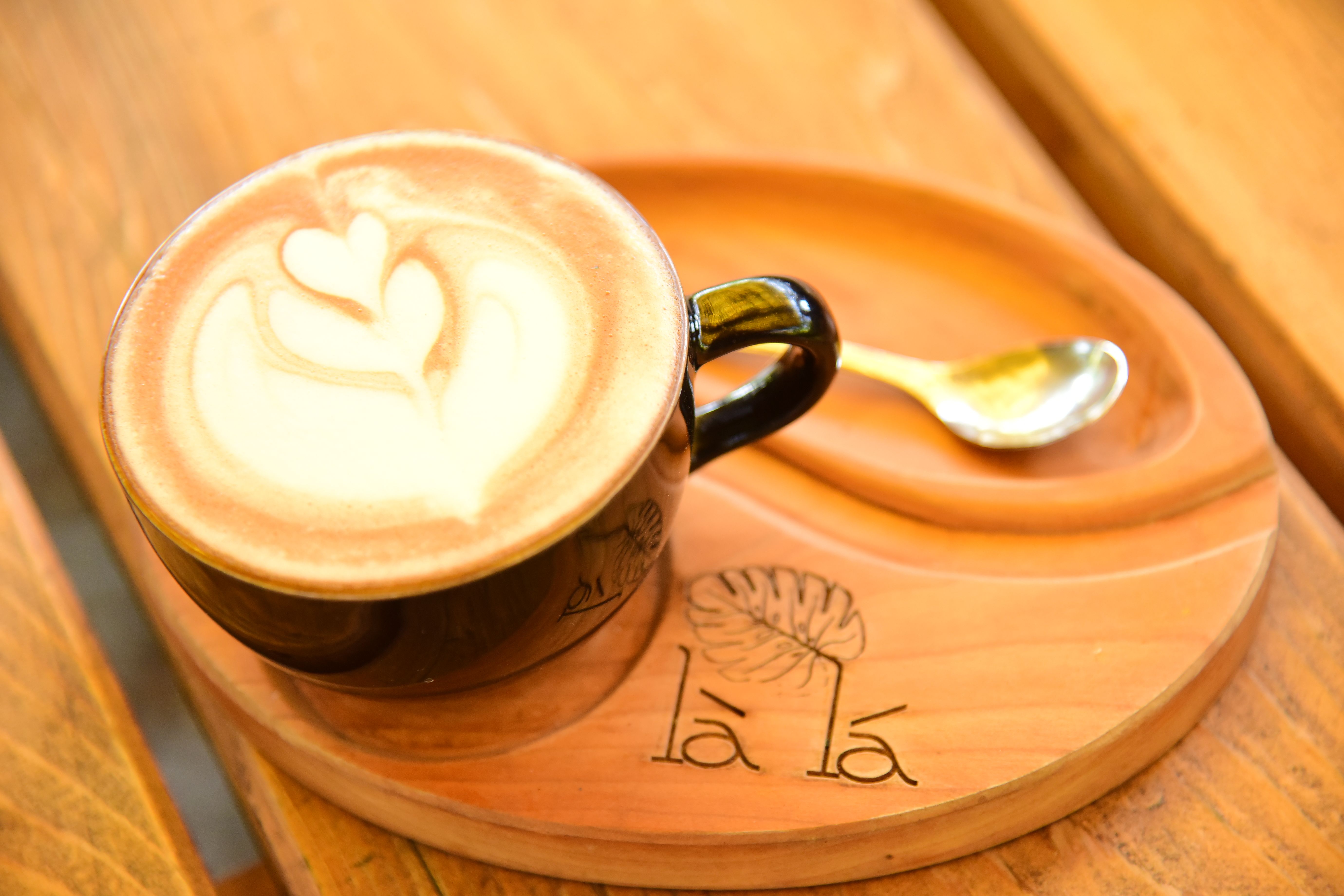 A beautifully crafted latte with heart-shaped art in a black mug on a carved wooden tray.