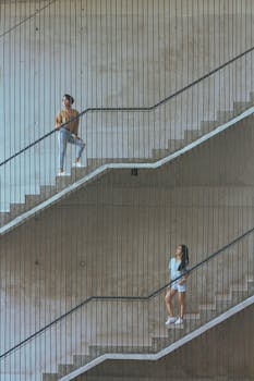 Two young adults posing on an outdoor staircase, showcasing modern fashion and architecture.