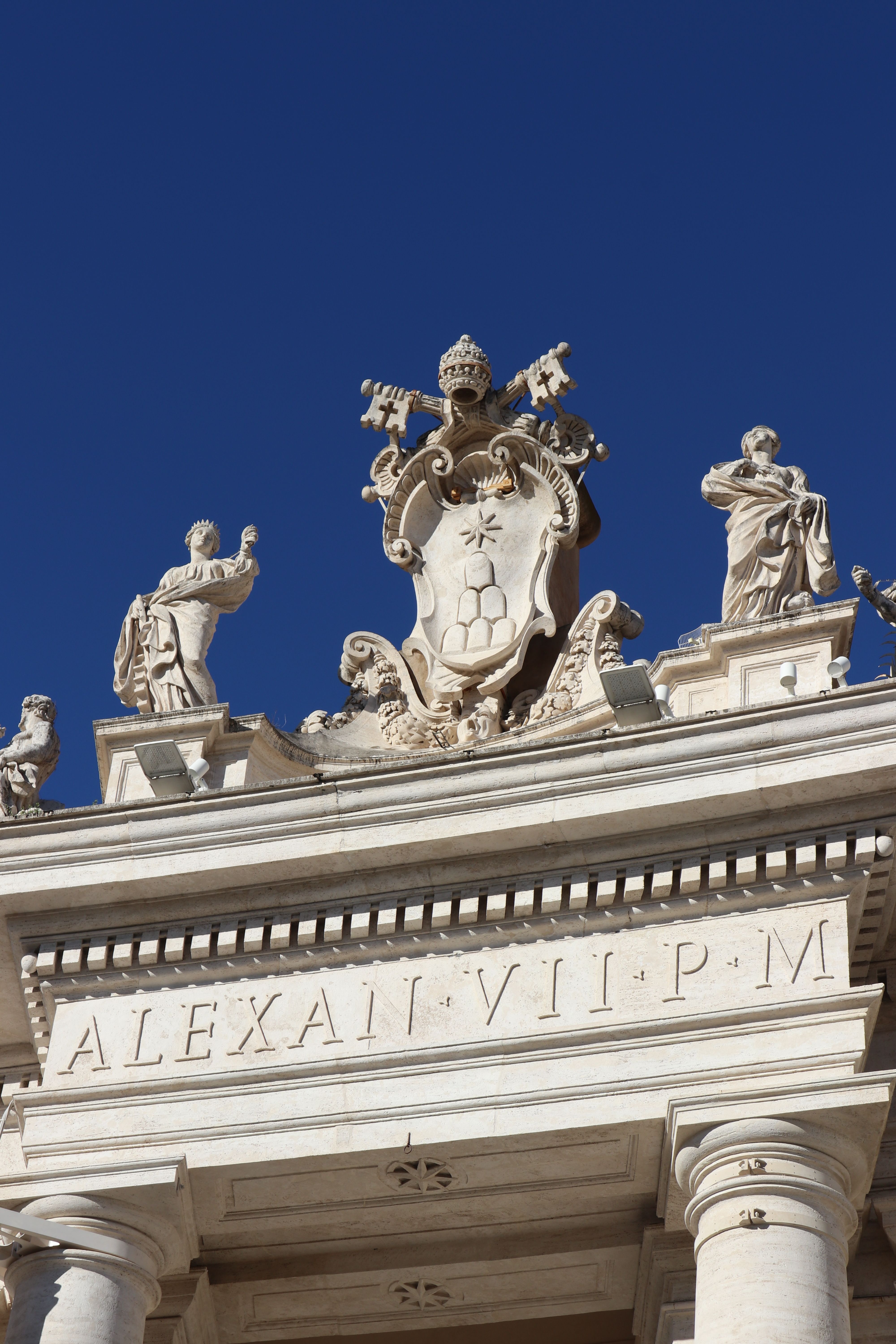 An intricate marble sculpture atop a historic Vatican City structure under a vivid blue sky.