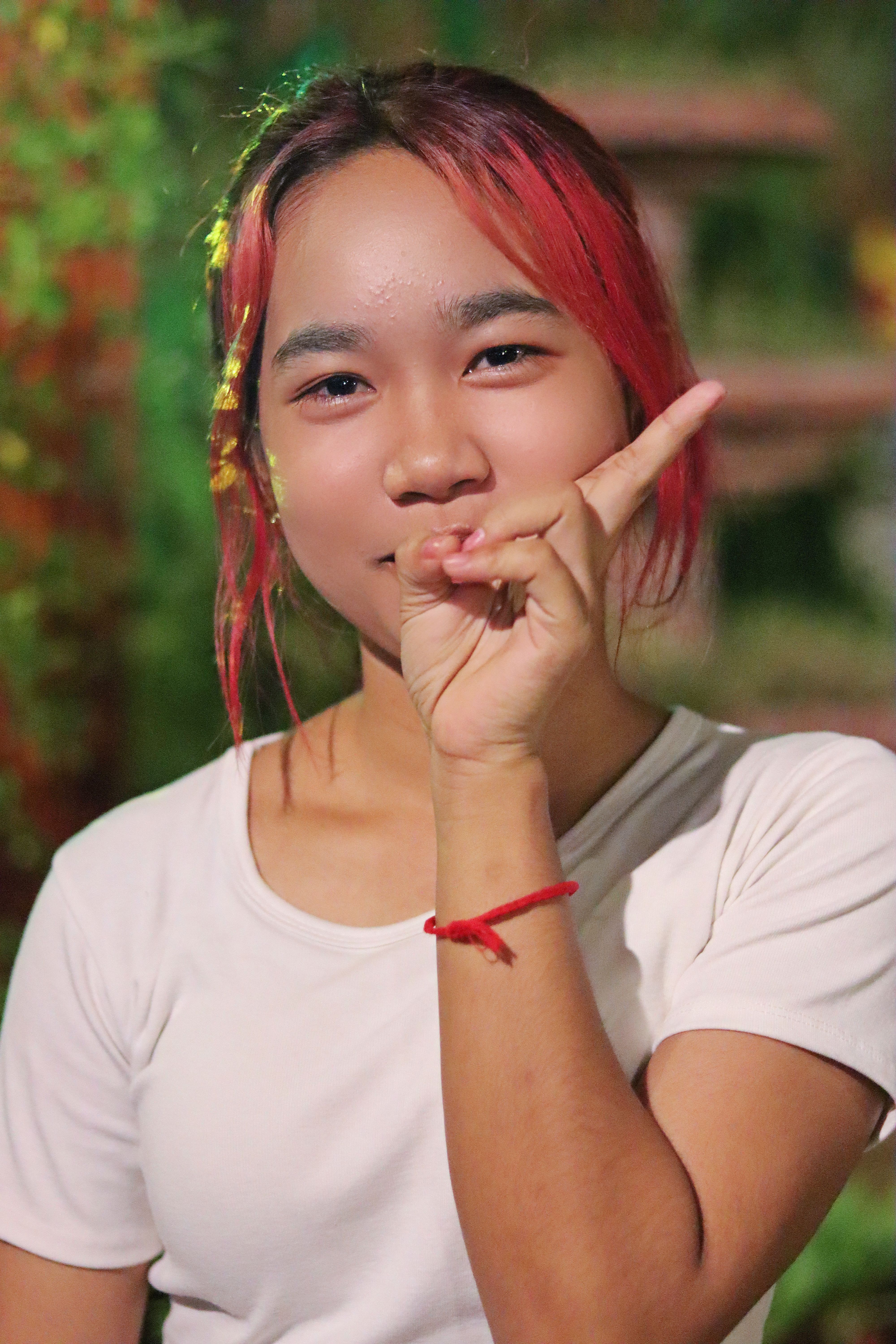 Playful young woman with red hair making a peace sign gesture outdoors.