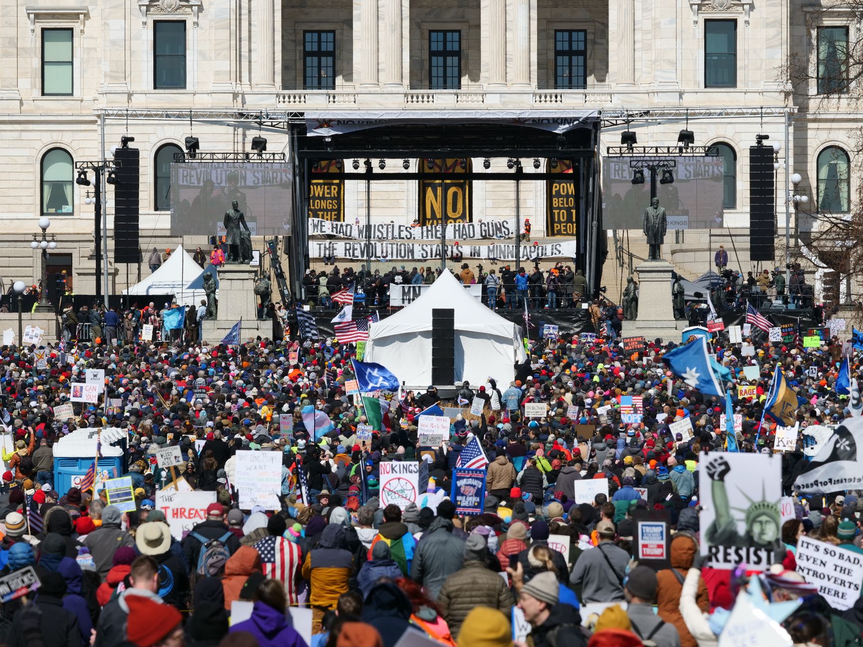 A large crowd gathers for a protest at the Minnesota State Capitol in Saint Paul, featuring signs and banners.