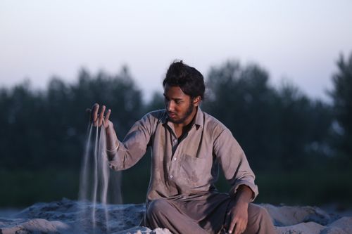 Free A man sitting outdoors sifting sand through his fingers at twilight, evoking contemplation. Stock Photo