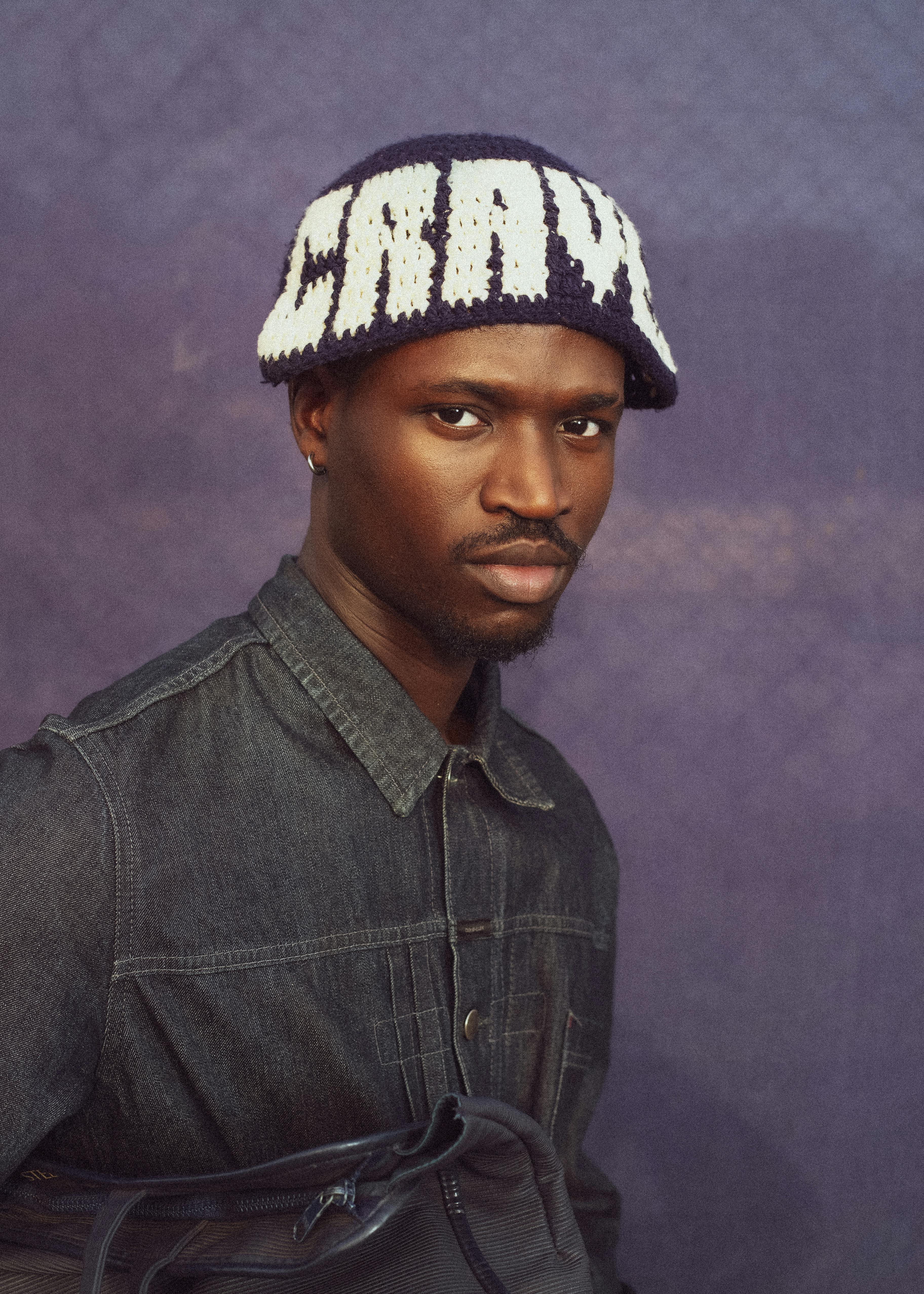 Stylish portrait of a man in a denim jacket with a knitted hat featuring text.