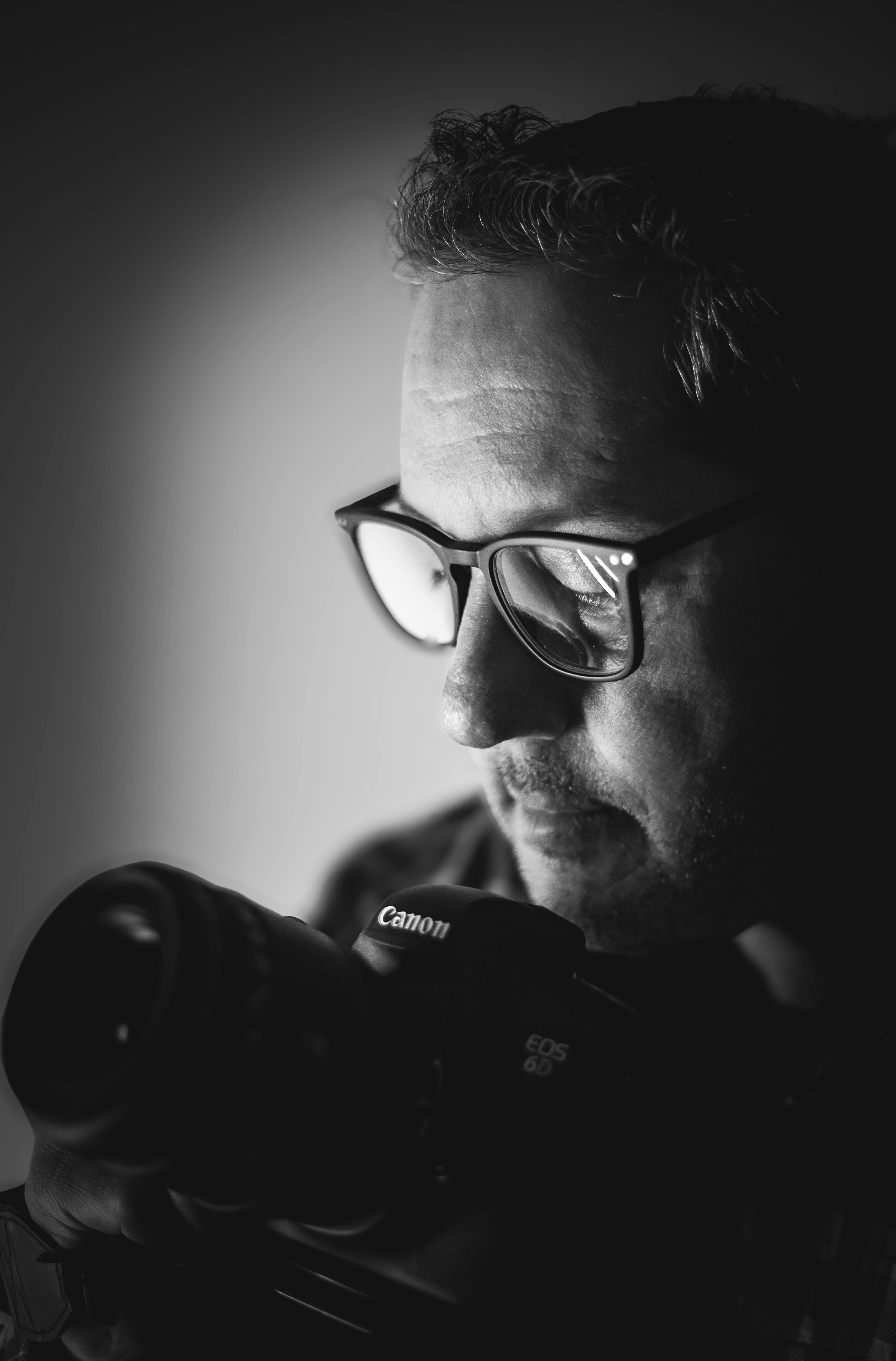 A focused photographer holding a camera, captured in dramatic black and white lighting.