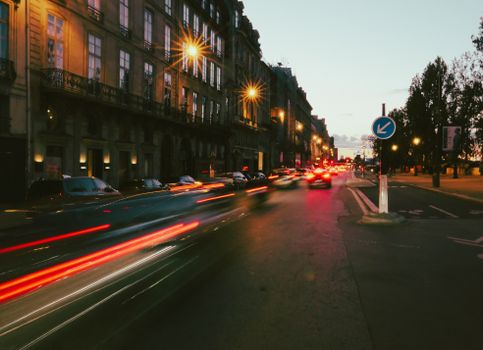 Long exposure of vibrant evening traffic on a street in Paris, capturing urban motion blur and city lights.