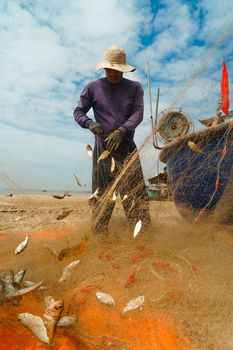 A fisherman removes fish from a net on Vũng Tàu Beach, showcasing traditional Vietnamese coastal life.