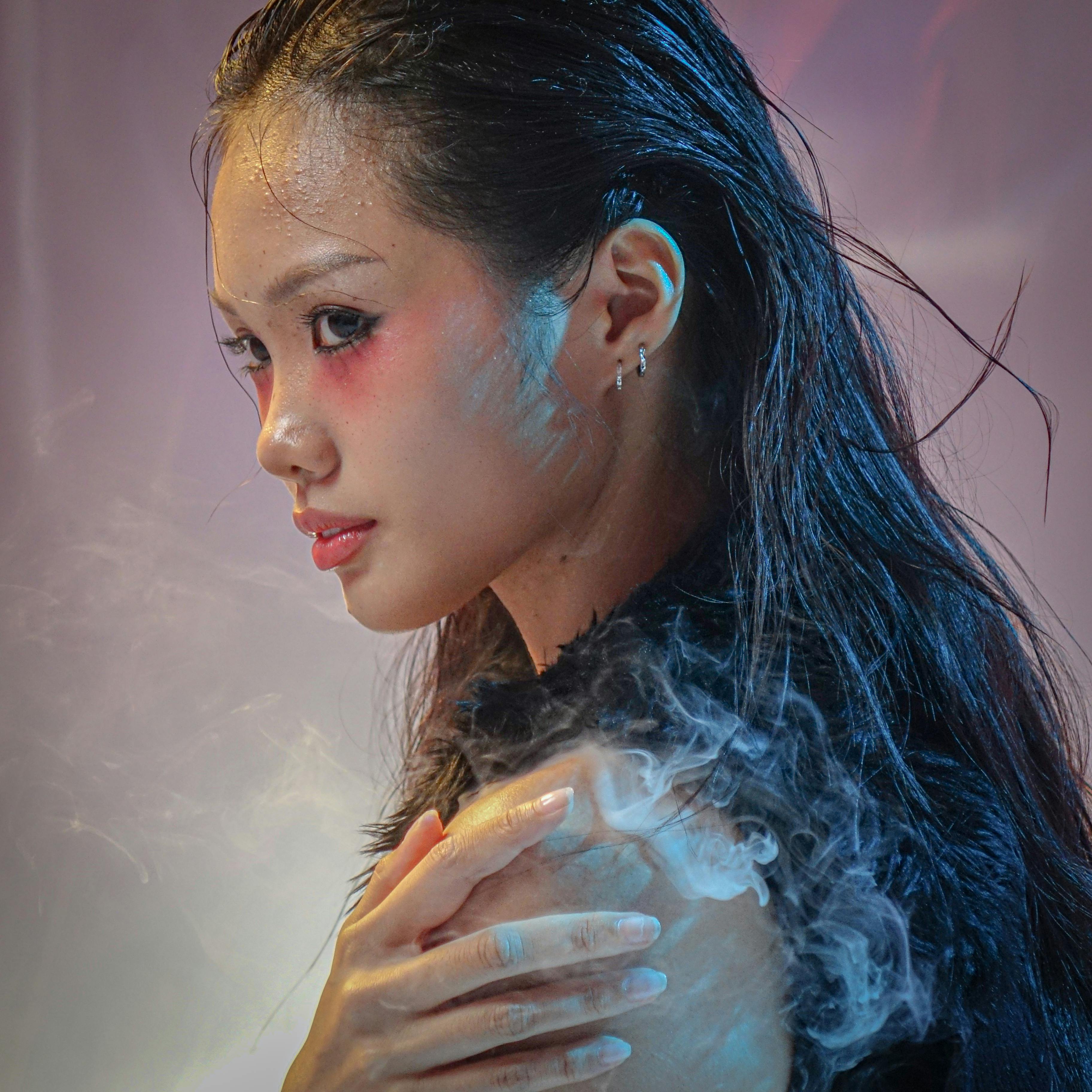 Artistic portrait of a person with smoky effects, showcasing vivid makeup and moody lighting.