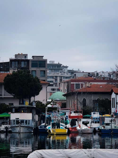 Free Tranquil harbor with colorful boats docked by a bustling cityscape under a cloudy sky. Stock Photo