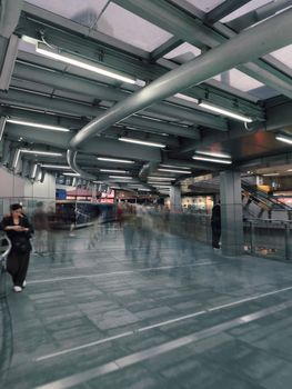 Blurred people moving along a contemporary covered walkway in bustling Bangkok.