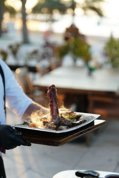 Elegant presentation of a sizzling steak by a chef at an outdoor restaurant, showcasing gourmet dining ambiance.