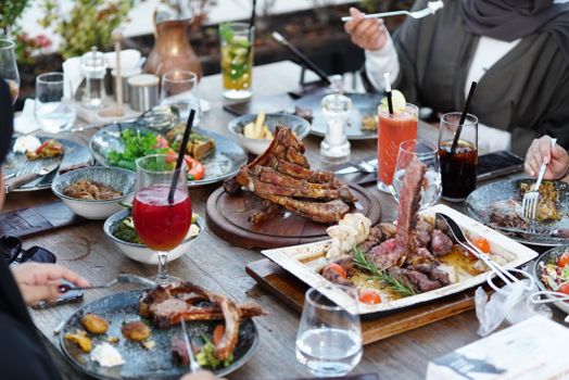 Friends enjoy a casual outdoor dining experience with a variety of grilled meats and colorful cocktails.