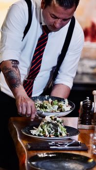 Chef in a white shirt and tie serves fresh salads. Professional dining experience.