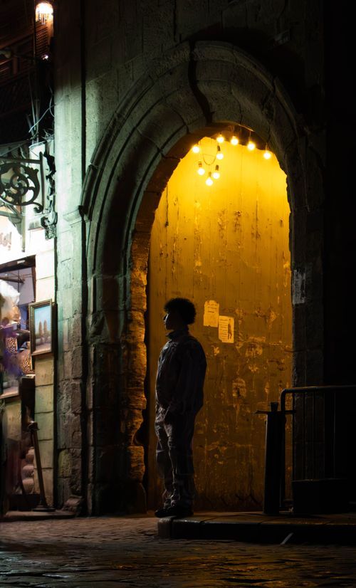 Free A silhouette of a person standing under an illuminated archway at night, creating a mysterious atmosphere. Stock Photo