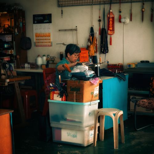 Free Elderly woman working at sewing machine inside traditional Malaysian shop, showcasing local craftsmanship. Stock Photo