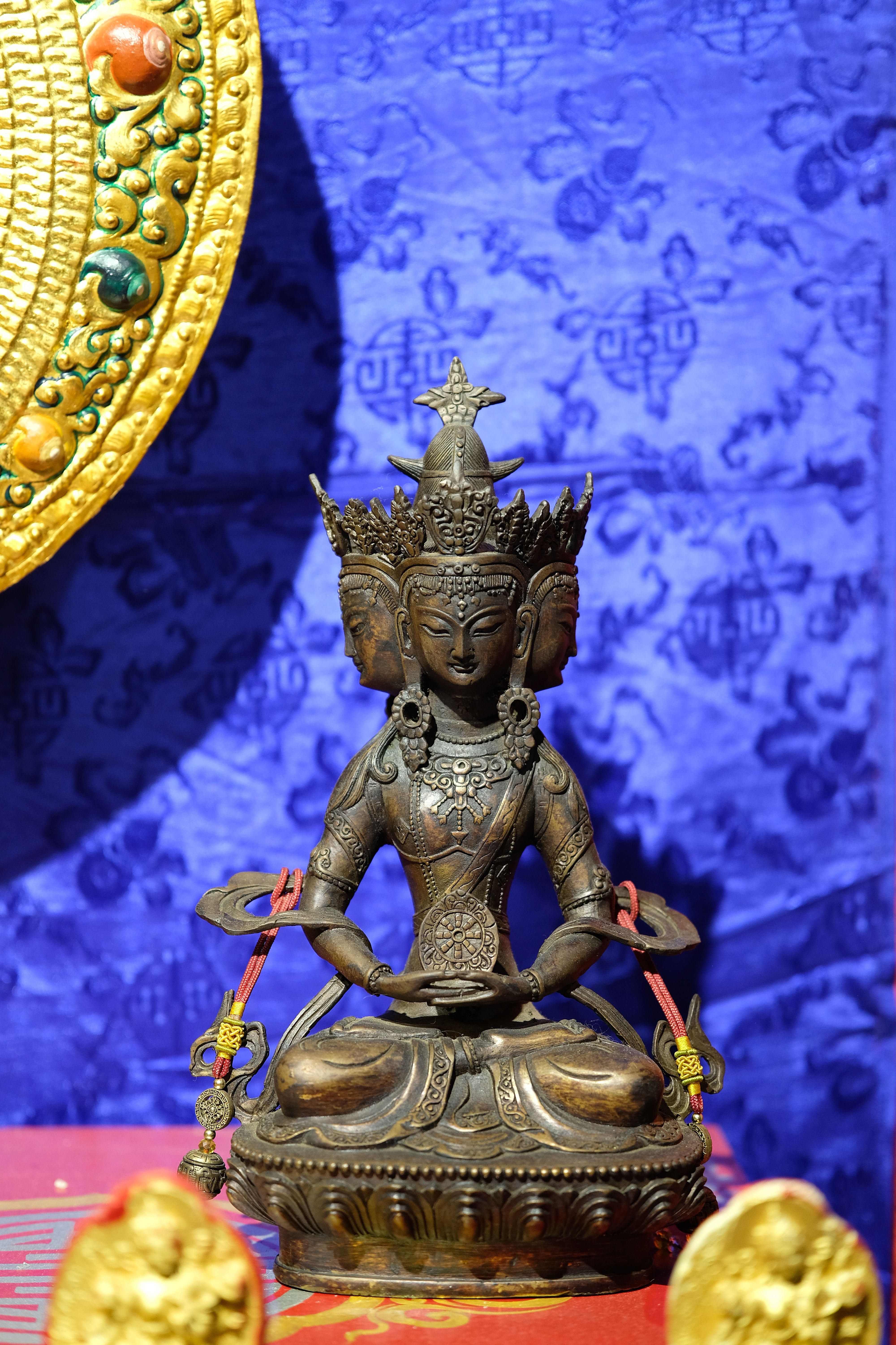 Bronze Buddha statue with ornate details and a vibrant blue tapestry background.