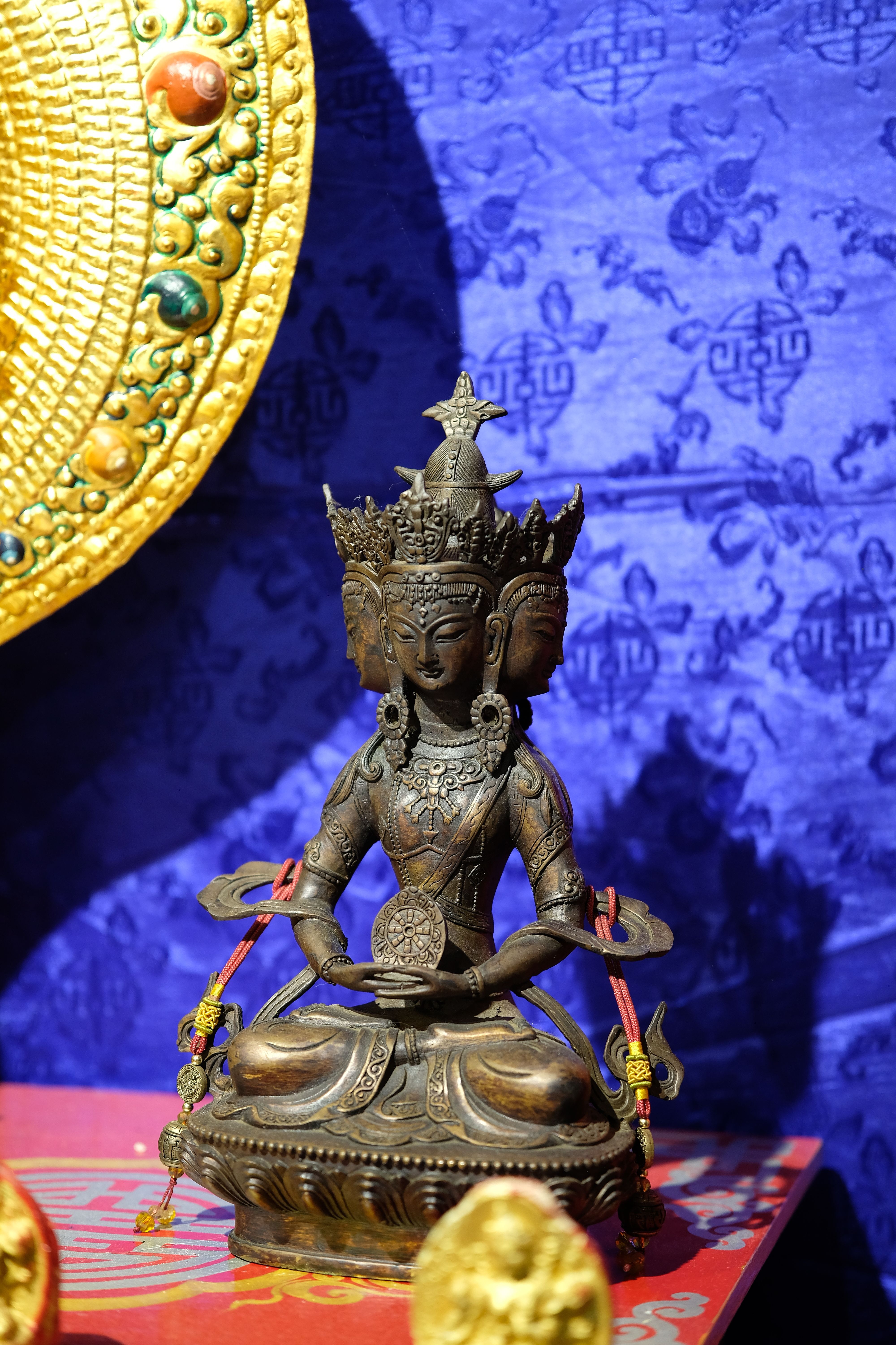 A detailed bronze statue of a Buddhist deity on a colorful, ornate background.