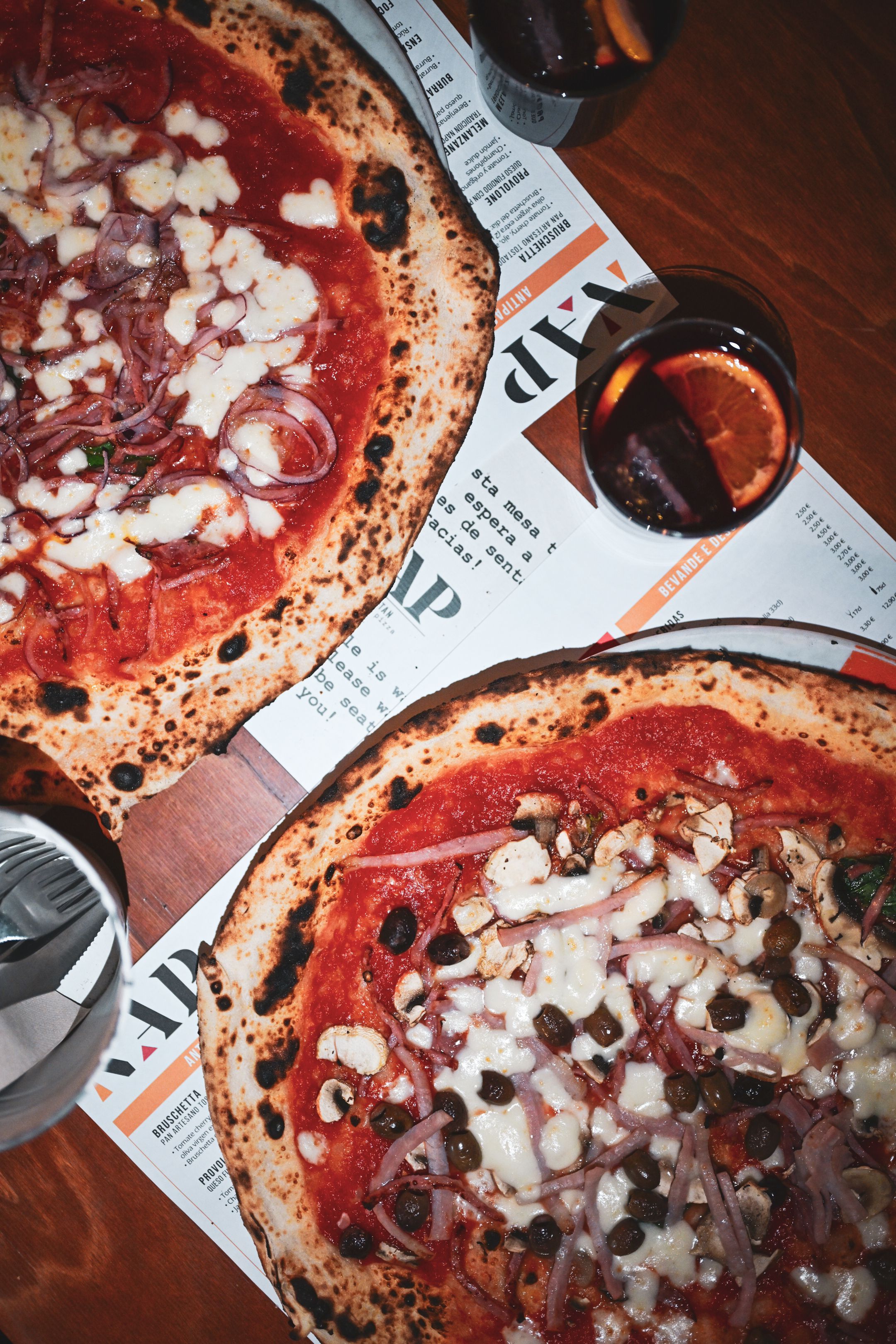 Two Neapolitan pizzas with toppings served on a wooden table in a cozy setting.