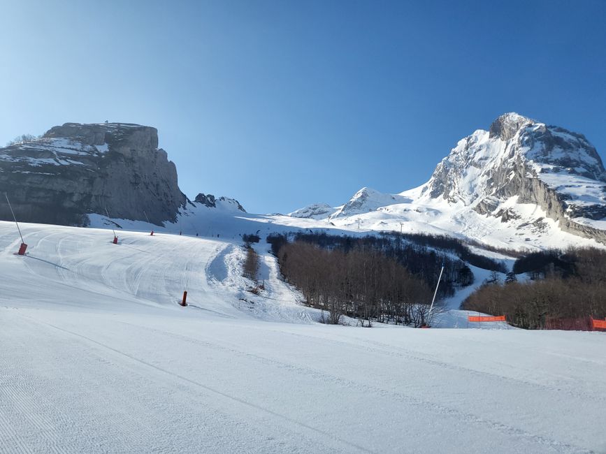 Serene snowy ski slope with majestic mountains under clear blue sky, perfect for winter sports.