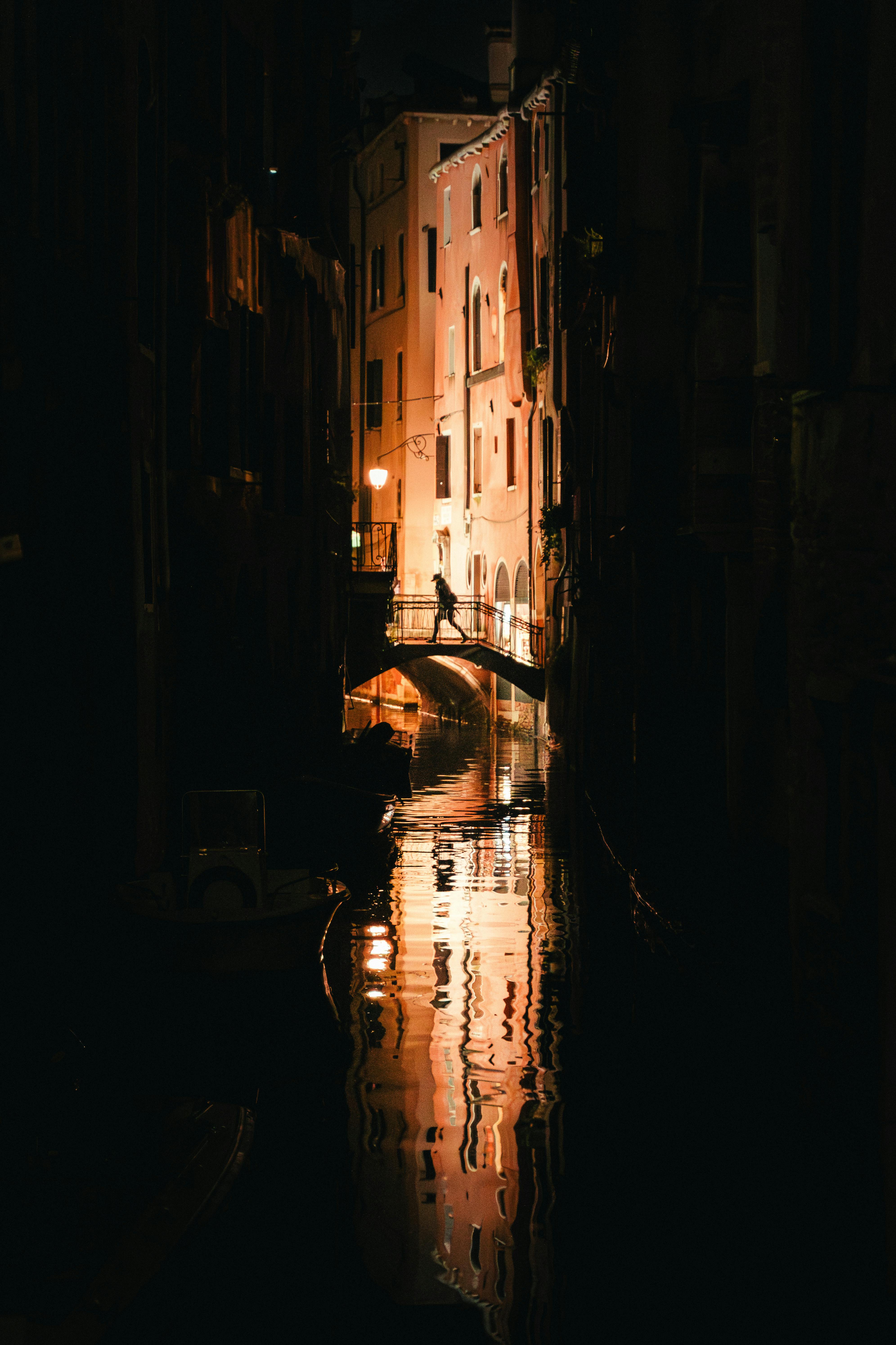 Stunning night view of a Venice canal with a silhouette of a bridge reflected in the water.