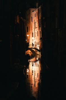 Stunning night view of a Venice canal with a silhouette of a bridge reflected in the water.
