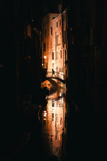 Stunning night view of a Venice canal with a silhouette of a bridge reflected in the water.