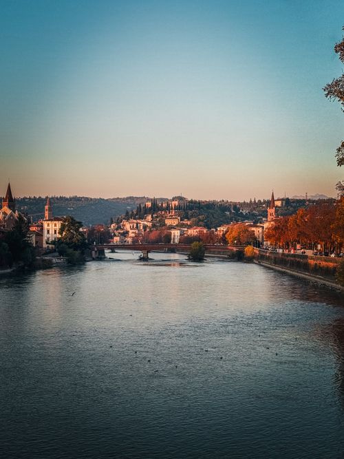 Free Scenic sunset over the Adige River in Verona, highlighting autumn colors and historic architecture. Stock Photo
