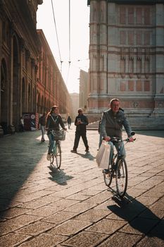 Sunlit street in Bologna with cyclists and historic architecture.