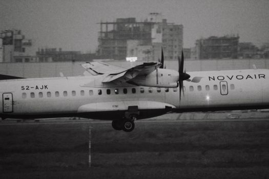 Black and white photo of a Novoair plane touching down with a cityscape backdrop.