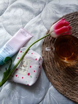 A relaxing flat lay featuring tea, a tulip, and skincare essentials on a woven mat.