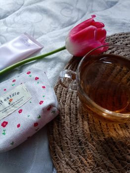 A serene indoor scene featuring a teacup, tulip, and fabric pouch on a woven mat.