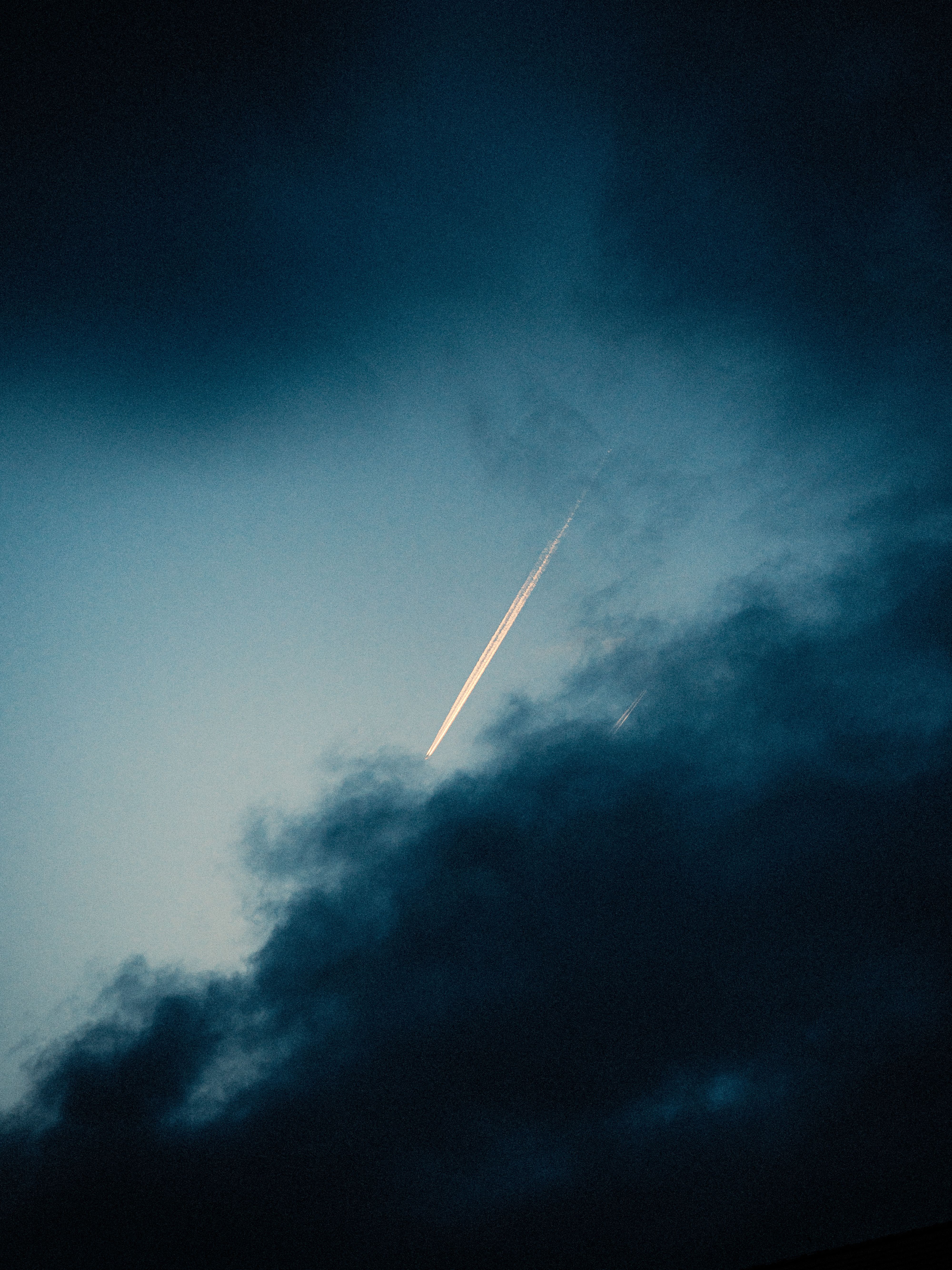 A dramatic twilight sky with a bright contrail illuminating through dark clouds.